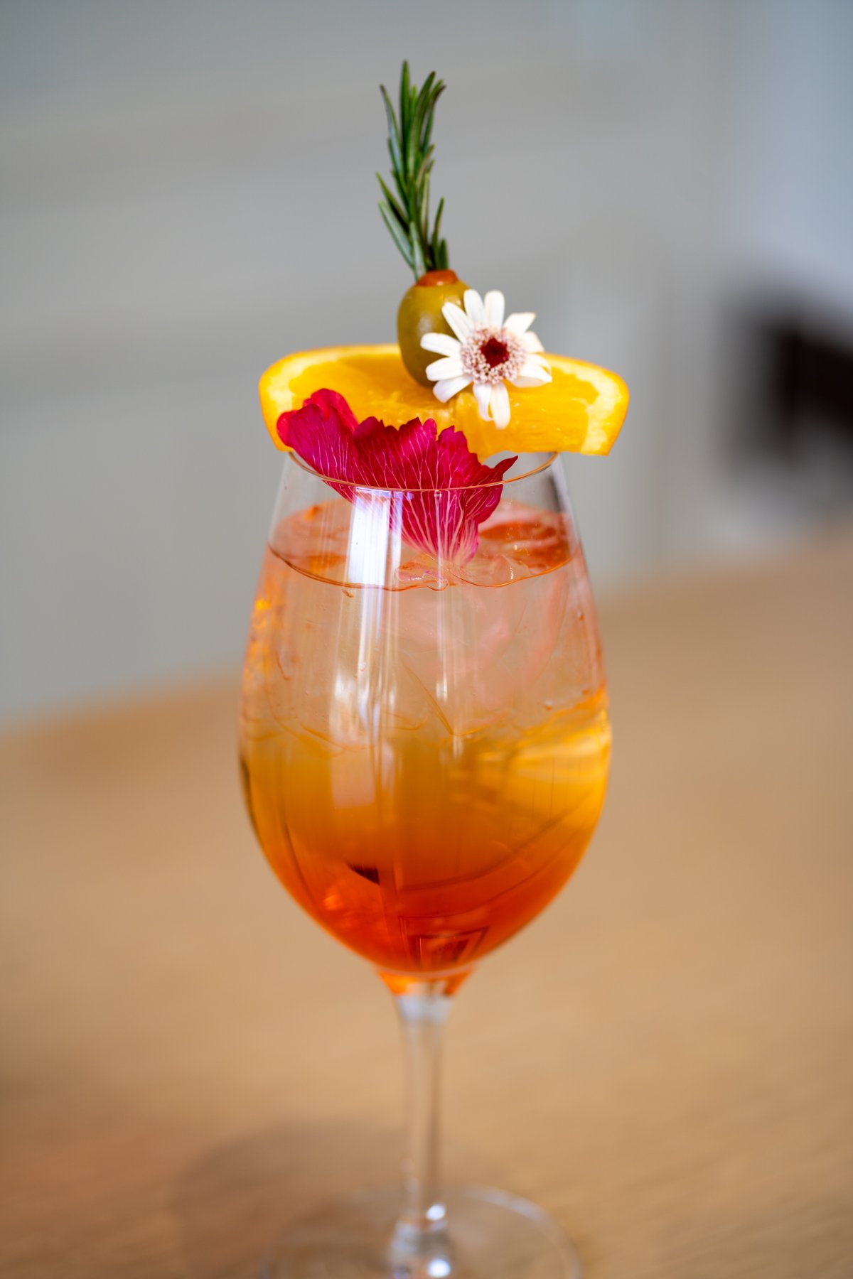 Orange cocktail with a floral garnish and rosemary sprig